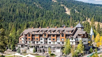 Un hotel de varios pisos con fachada de piedra, varios balcones y un complejo de esquí al fondo.