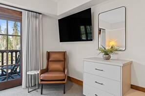 Une chambre d’hôtel avec un fauteuil en cuir marron, une commode blanche, un miroir et une fenêtre avec des rideaux.