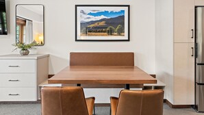 A modern dining area with a wooden table, two leather chairs, a white cabinet with drawers, a framed landscape picture on the wall, and a refrigerator. - Happy Loon | Includes Two 1-Day Lift Tickets (Tamarack)