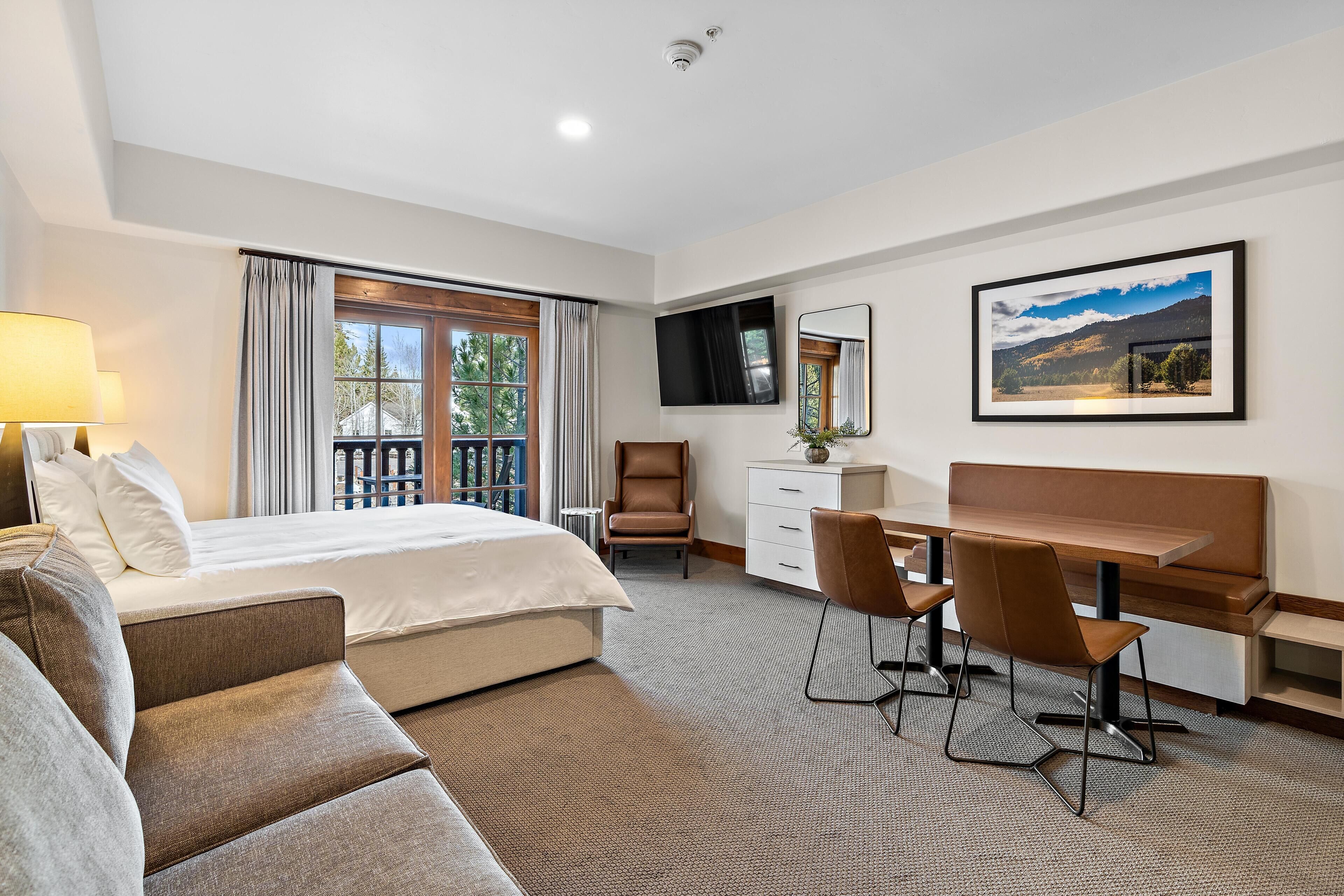 A hotel room with a bed, a desk, a chair, a sofa, a TV, and a window with curtains.
