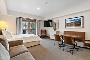 A hotel room with a bed, a desk, a chair, a sofa, a TV, and a window with curtains.