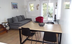 A compact living space with a dining table, two chairs, a red chair, a grey sofa, and a small side table.