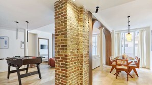Een ruime woonkamer met een schouw van baksteen, een tafelvoetbaltafel en een eettafel gedekt voor zes personen.