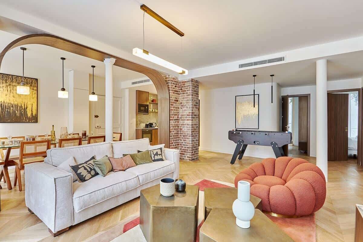 Ein modernes Wohnzimmer mit einem weißen Sofa, einem roten Sitzhocker und einem Kicker.