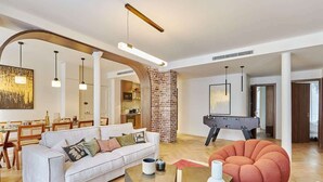 Een moderne woonkamer met een witte bank, een rode poef en een tafelvoetbal.