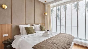 Een moderne slaapkamer met een groot bed, een nachtkastje en een raam met uitzicht op bomen.
