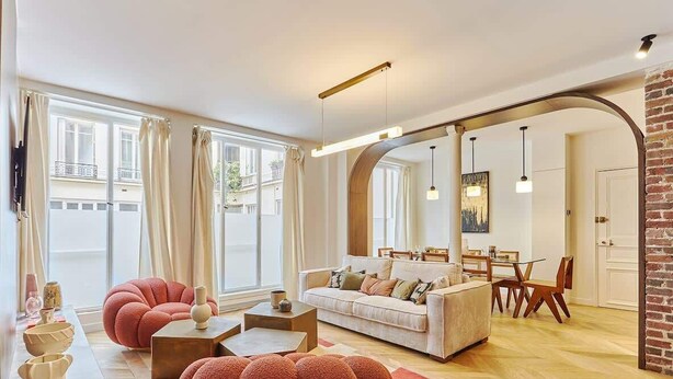 Een ruime woonkamer met een bank, fauteuils en een salontafel. Er is een eethoek met een tafel en stoelen.
