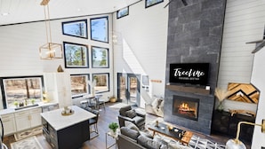 A spacious living area with a fireplace, large windows, and a modern kitchen. - Game-Filled Retreat for Families and Friends (Broken Bow)