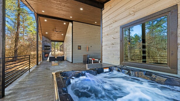 A wooden deck with a hot tub, wooden walls, and a large window overlooking trees. - Game-Filled Retreat for Families and Friends (Broken Bow)