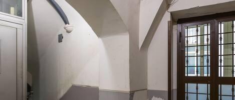 A hallway with a marble floor, a door with a metal grid, and a white wall with a visible pipe.