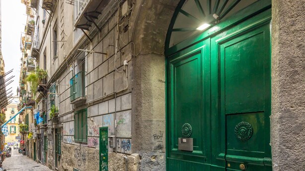 Uma rua estreita de paralelepípedos, com uma porta verde e uma parede de pedra.