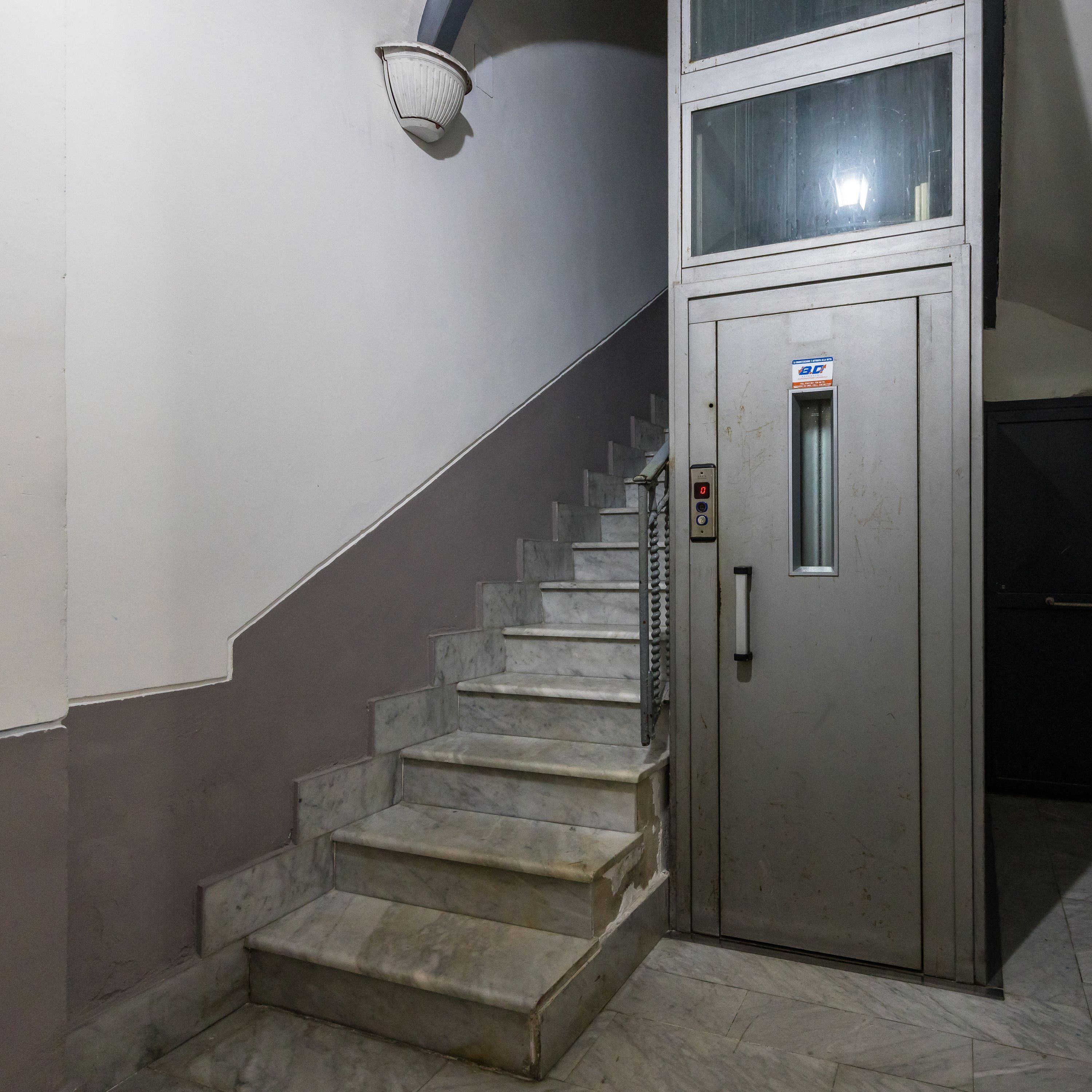 A staircase leading to a metal elevator with a digital display.