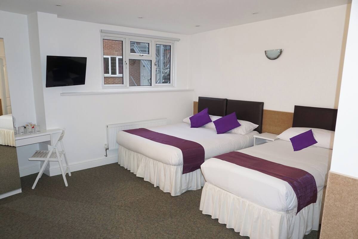 A hotel room with two beds, a desk, and a TV.