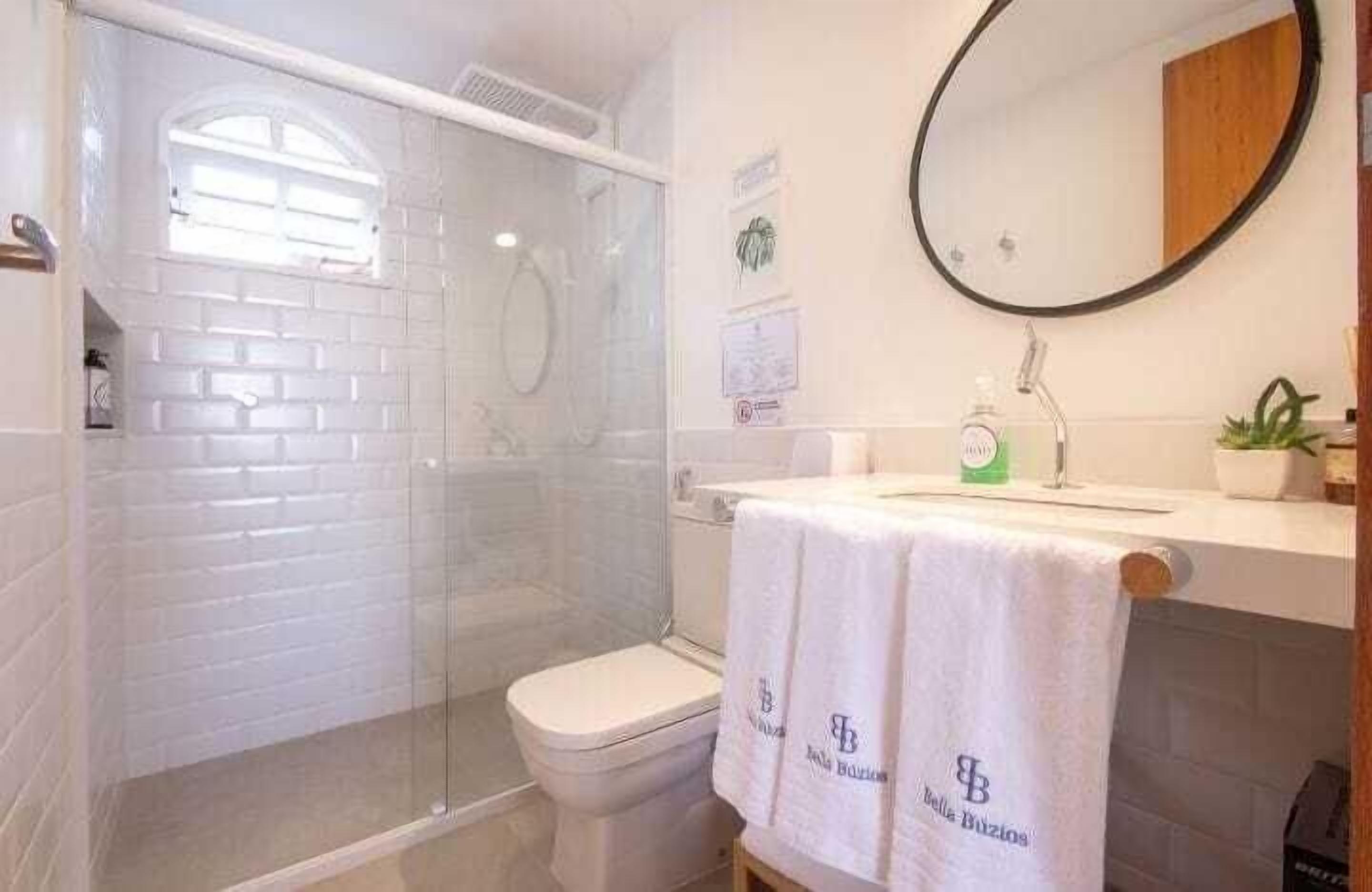 A bathroom with a glass-enclosed shower, a toilet, a sink with a mirror, and a towel with a logo.