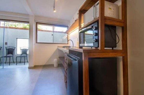 Cocina compacta con microondas, lavavajillas y estantes de madera. Hay una puerta corrediza de vidrio que da a un espacio exterior con sillas.