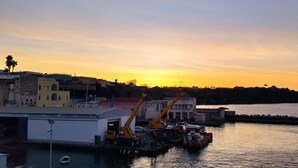Une zone industrielle située au bord de l’eau, avec des bâtiments, des grues et un quai, le tout baigné par les couleurs du coucher de soleil.