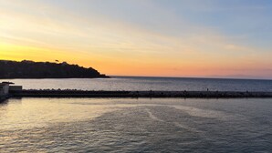 Un paysage côtier avec une mer calme, une côte rocheuse et un ciel dégagé au coucher du soleil.