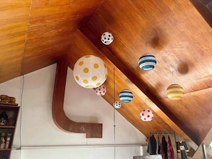 Ein modernes Interieur mit Holzbalkendecke, einer großen weißen Wand mit geometrischem Muster und hängenden, kugelförmigen Lampen mit Punkten.