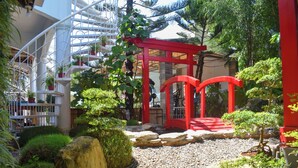 A garden with a red gate, a white spiral staircase, and various plants. - Orokasa Guesthouse (Puerto Princesa)