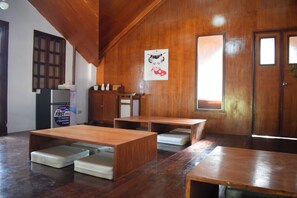 Ein Zimmer mit Holzwänden, einer traditionellen japanischen Tür und einem Poster einer Geisha. Holzische und -bänke stehen hier, und in der Ecke ist ein Kühlschrank zu sehen.