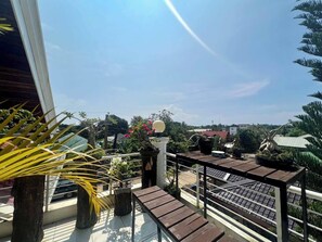 Ein Balkon mit Blumentöpfen, einem Holztisch und Blick auf die umliegende Nachbarschaft.