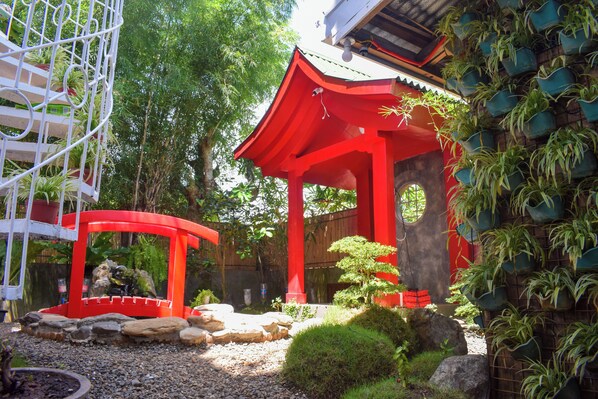 A traditional Japanese structure with a red roof, surrounded by greenery and rocks.