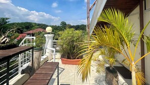 A rooftop terrace with a view of a red-roofed building, a white spherical object, and various potted plants. - Orokasa Guesthouse (Puerto Princesa)