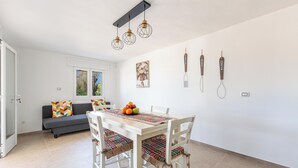 A dining area with a white table, chairs, and a patterned table runner. There is a gray sofa with colorful pillows in the background.