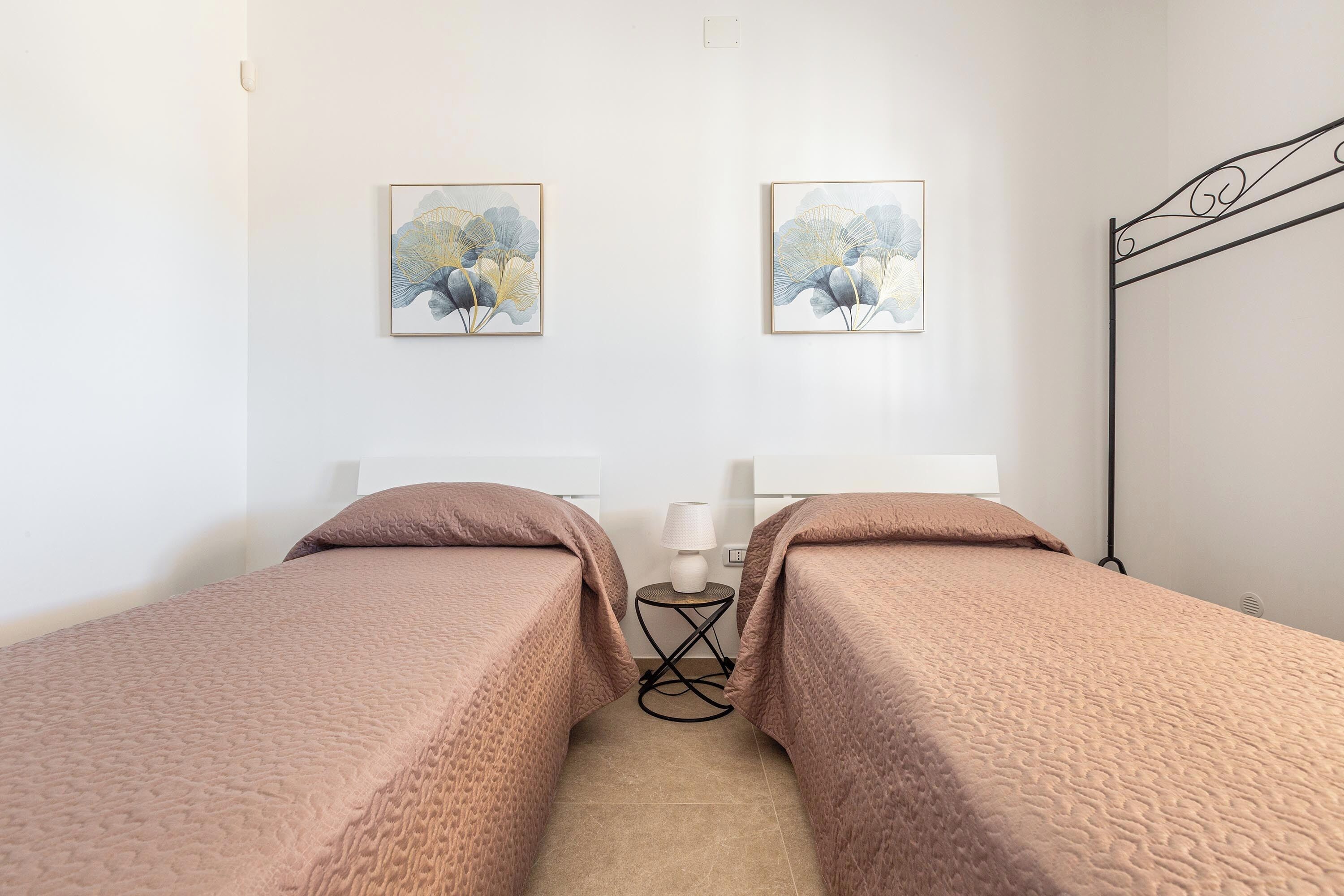 Een kamer met twee bedden, een nachtkastje met een lamp en twee kunstwerken in lijsten aan de muur.