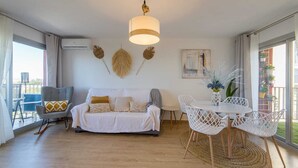 A modern living room with a sofa, chairs, a dining table, and a hanging light fixture. - Apartamento Lake & SEA (Valencia)