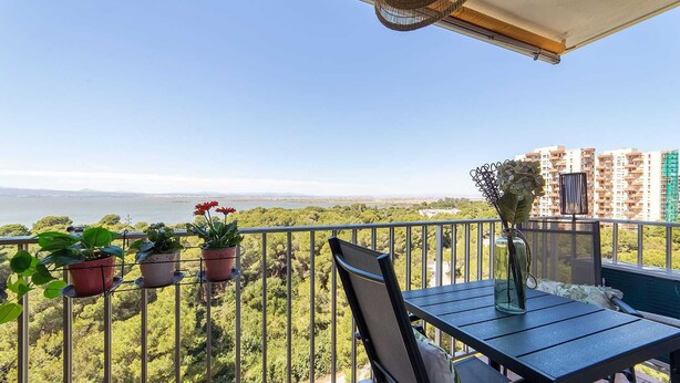 A balcony with a table and chairs, potted plants, and a view of a body of water and buildings. - Apartamento Lake & SEA (Valencia)