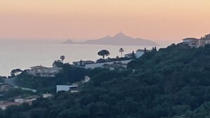 Een kustlandschap met uitzicht op zee en verre bergen.
