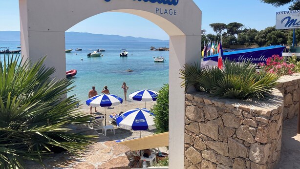 Een boog die de toegang tot het strand markeert, met de naam "Marinella Plage" en een bord voor een restaurant.
