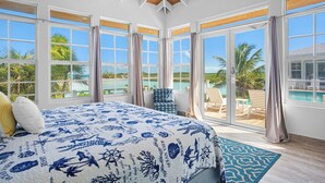 A bedroom with a large bed, multiple windows, and a view of a pool and palm trees. - BEACHFRONT! Best Location on Private Lazy River Sand Bar.  Always Calm Water! (Moore Hill)
