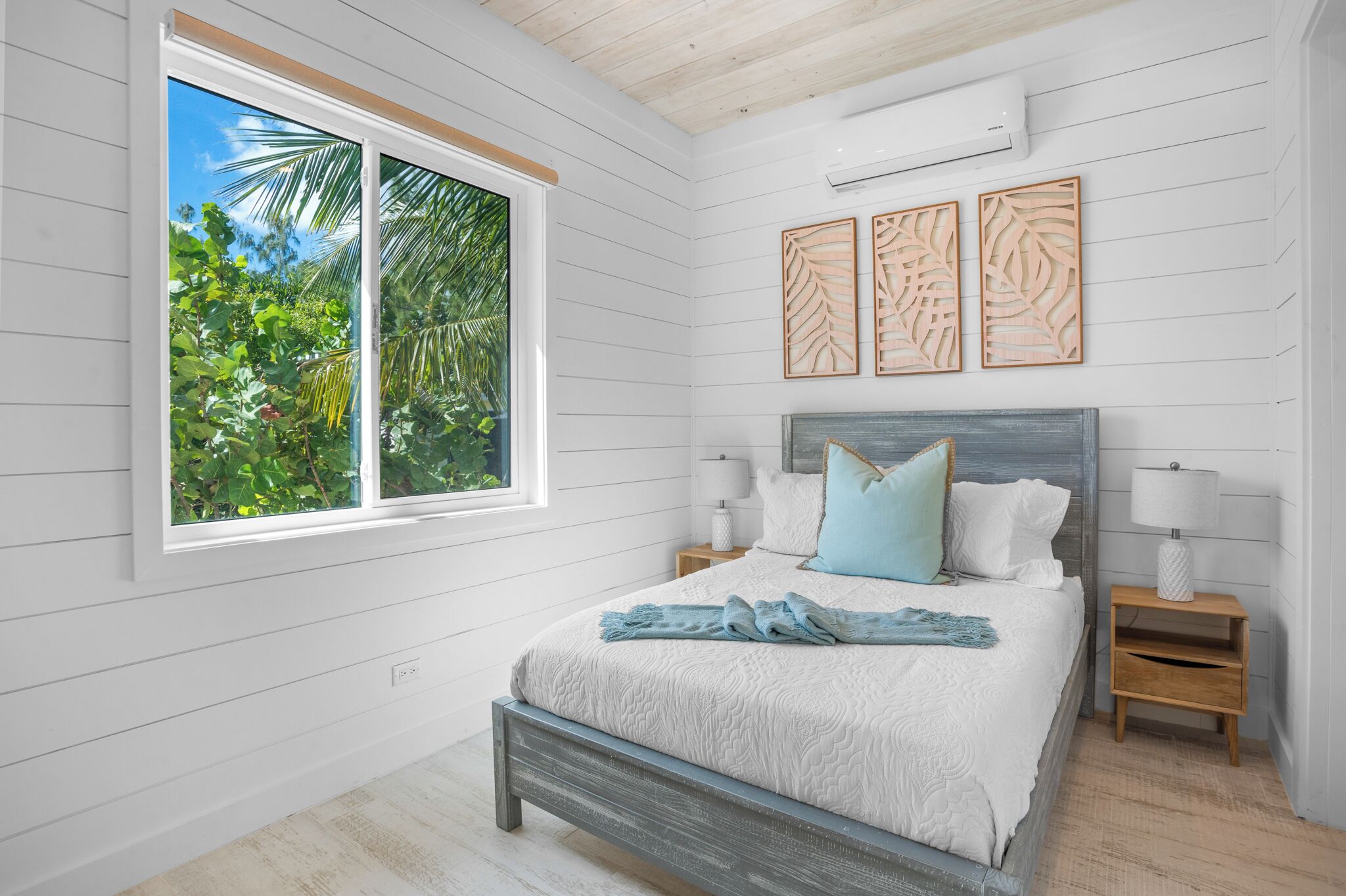 A bedroom with a bed, bedside tables, a window with a view of greenery, and wall art.