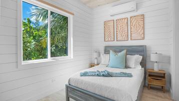 A bedroom with a bed, bedside tables, a window with a view of greenery, and wall art.