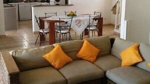 Een woonkamer met een bank en salontafel, een eethoek met tafel en stoelen, en een keuken op de achtergrond.
