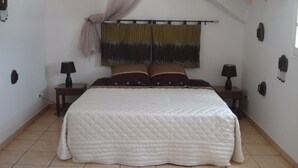 Een slaapkamer met een groot bed, twee nachtkastjes, een hangend gordijn en een aan de muur bevestigde telefoon.