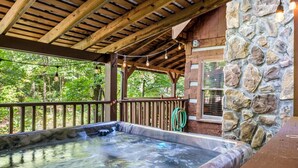 A hot tub under a wooden pergola with stone walls, surrounded by a wooden deck and a stone wall. - Secluded Cabin| A+ location <2M DT + Ober| Hot Tub| Firepit| Gameroom (Gatlinburg)