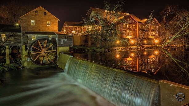 A historic building with a large water wheel and a wooden structure with illuminated windows. - Secluded Cabin| A+ location <2M DT + Ober| Hot Tub| Firepit| Gameroom (Gatlinburg)
