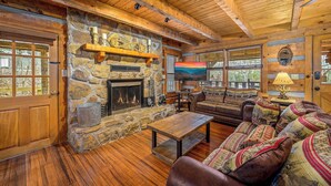 A cozy cabin interior with a stone fireplace, wooden floors, and a leather sofa with patterned cushions. - Secluded Cabin| A+ location <2M DT + Ober| Hot Tub| Firepit| Gameroom (Gatlinburg)
