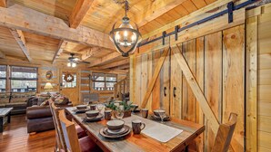 A wooden interior with a dining table set for six, a sofa, and a chandelier. - Secluded Cabin| A+ location <2M DT + Ober| Hot Tub| Firepit| Gameroom (Gatlinburg)