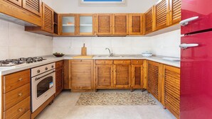 A kitchen with wooden cabinets, a gas stove, an oven, and a red refrigerator. - 3882 Residenza Virginia by Barbarhouse (Tricase)