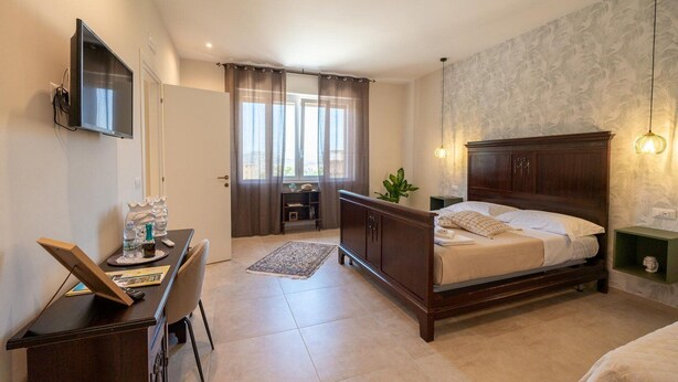 Un dormitorio con una cama de madera, un escritorio con una silla, un televisor y una ventana con cortinas.