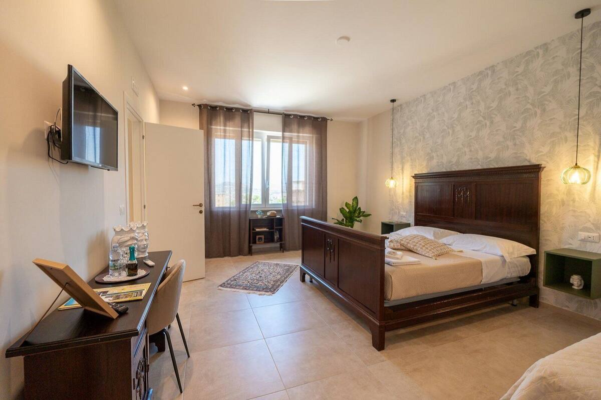 A bedroom with a wooden bed, a desk with a chair, a television, and a window with curtains.
