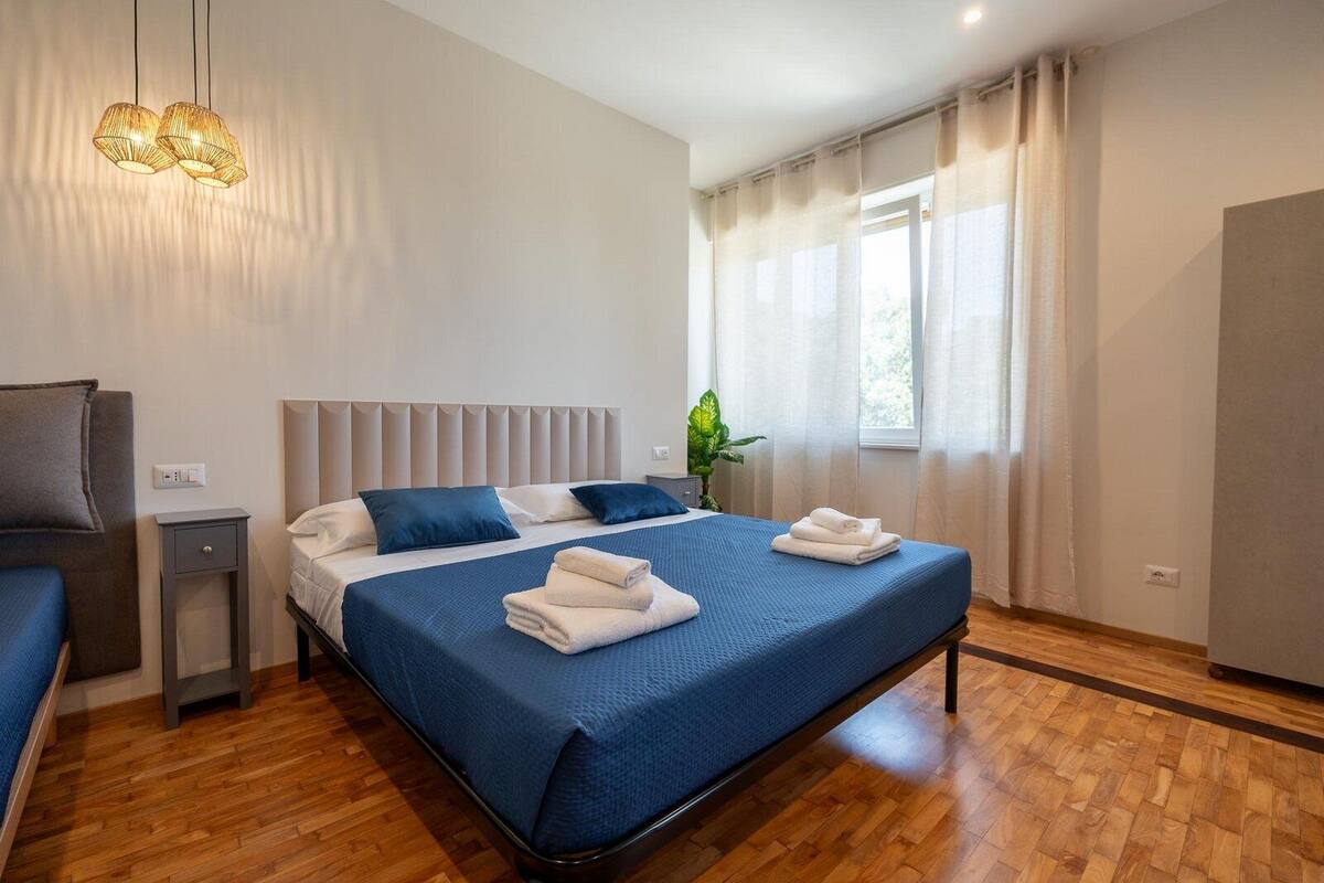A modern hotel room with a large bed, bedside tables, a desk, and a hanging light fixture.