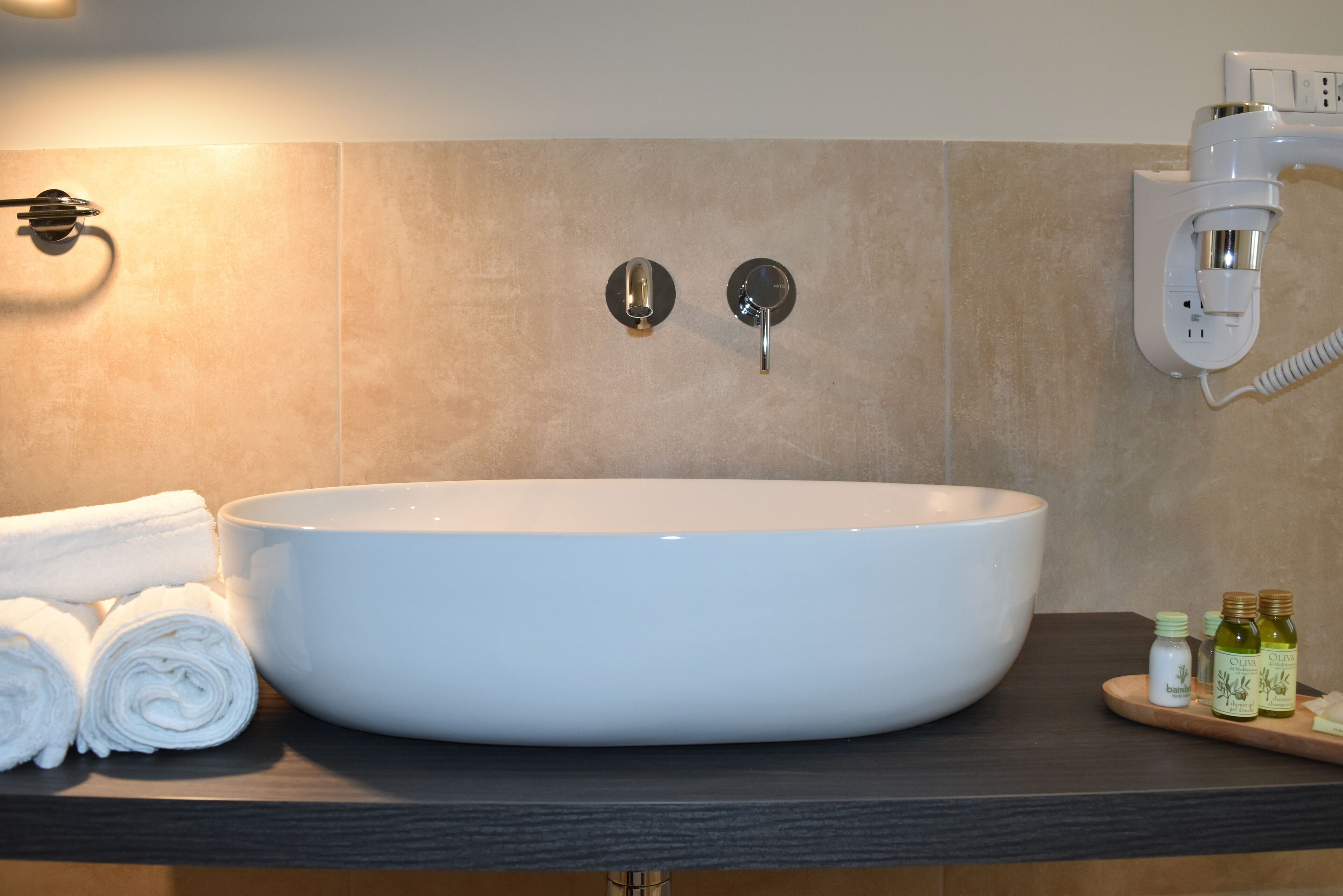 A bathroom with a large white sink, two wall-mounted towel dispensers, and a wall-mounted hairdryer.