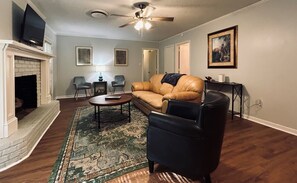 A living room with a fireplace, leather sofa, two armchairs, a coffee table, and a ceiling fan. - *King* Bed In Heart of City Close to the Reservoir (Jackson)