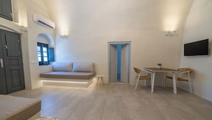 A modern living room with a built-in sofa, a dining table with chairs, a small side table, and a TV mounted on the wall. - Alaya Suites (Pyrgos)