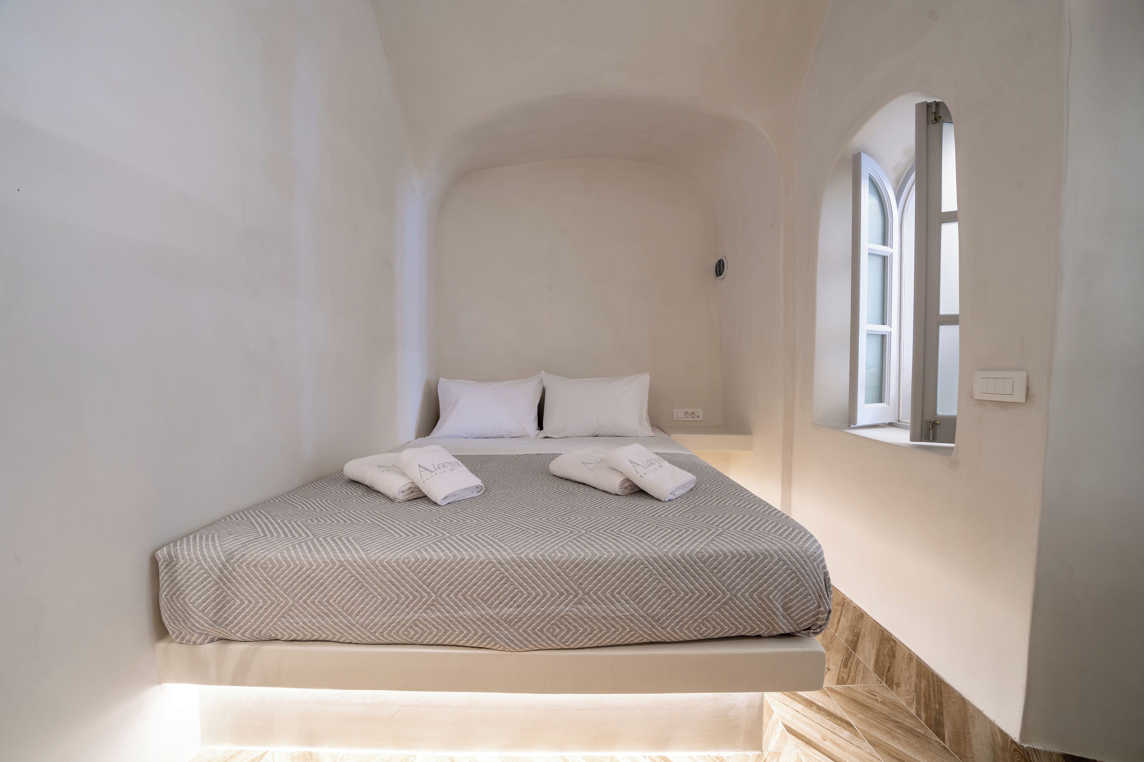 A bedroom with a bed, two pillows, a window, and a bedside table.